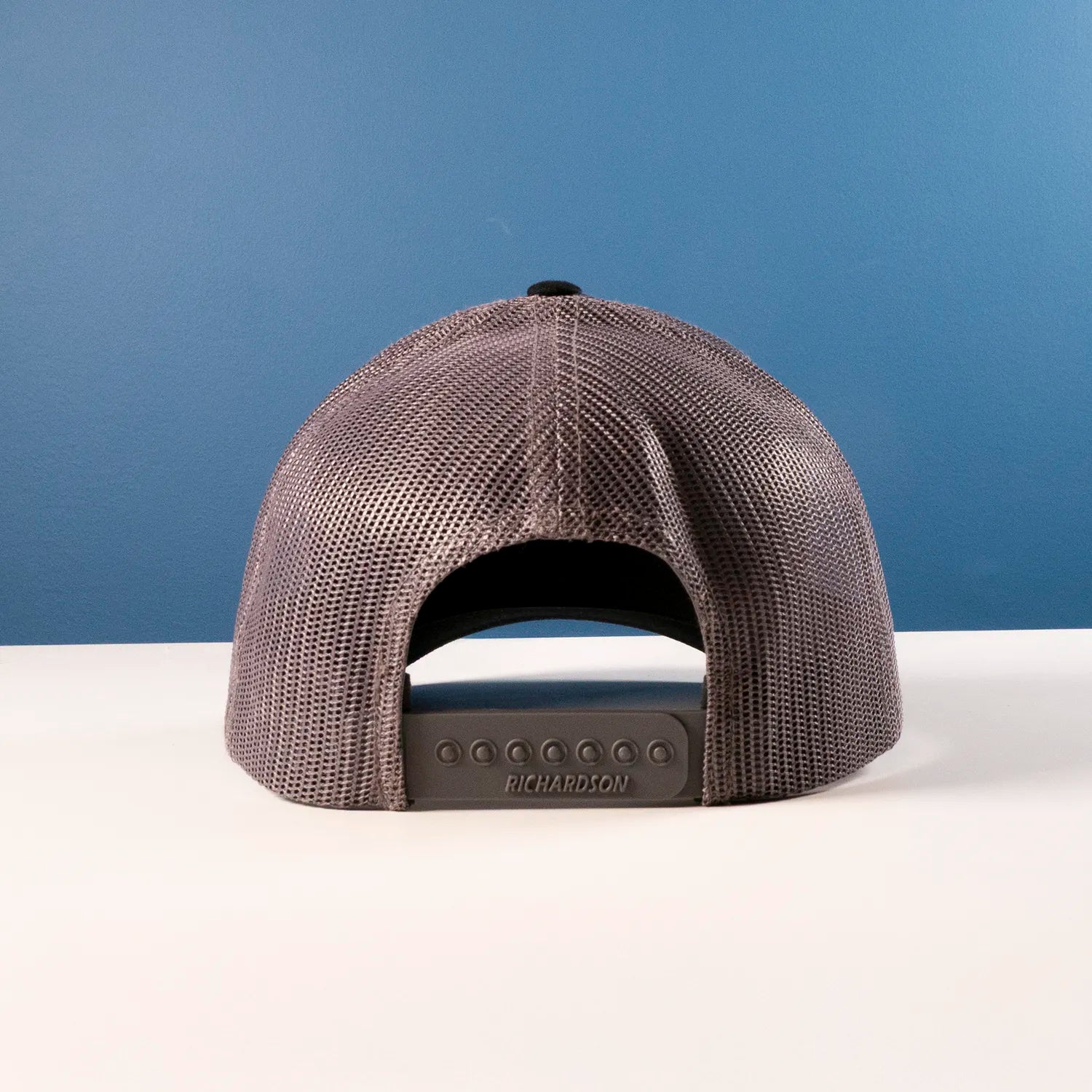 Black trucker cap with Richardson logo on a white surface and blue background